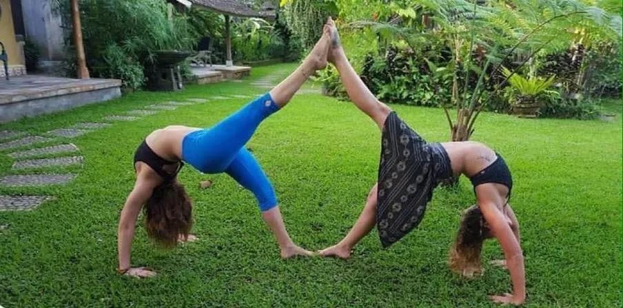 Two guests in mirrored yoga poses on the garden lawn at dusk