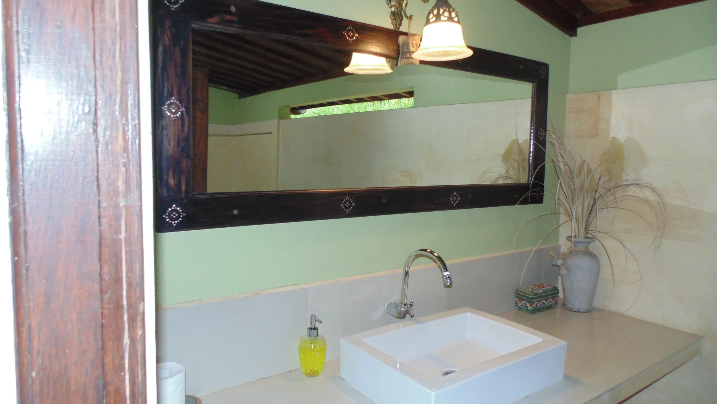En-suite vanity with a vessel sink, carved wooden mirror and dried grasses
