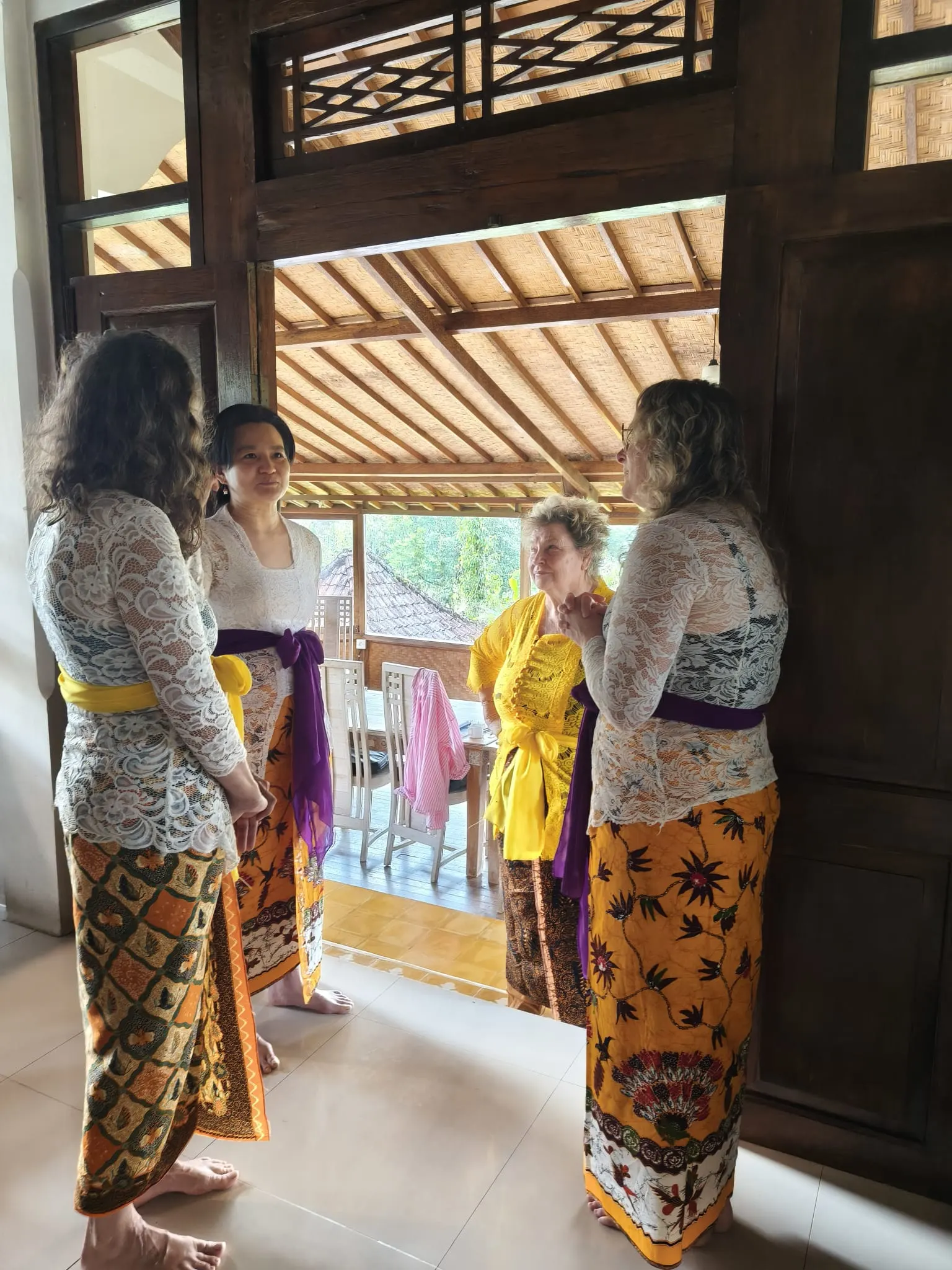 Guests in lace kebaya and batik talking in a tall carved timber doorway