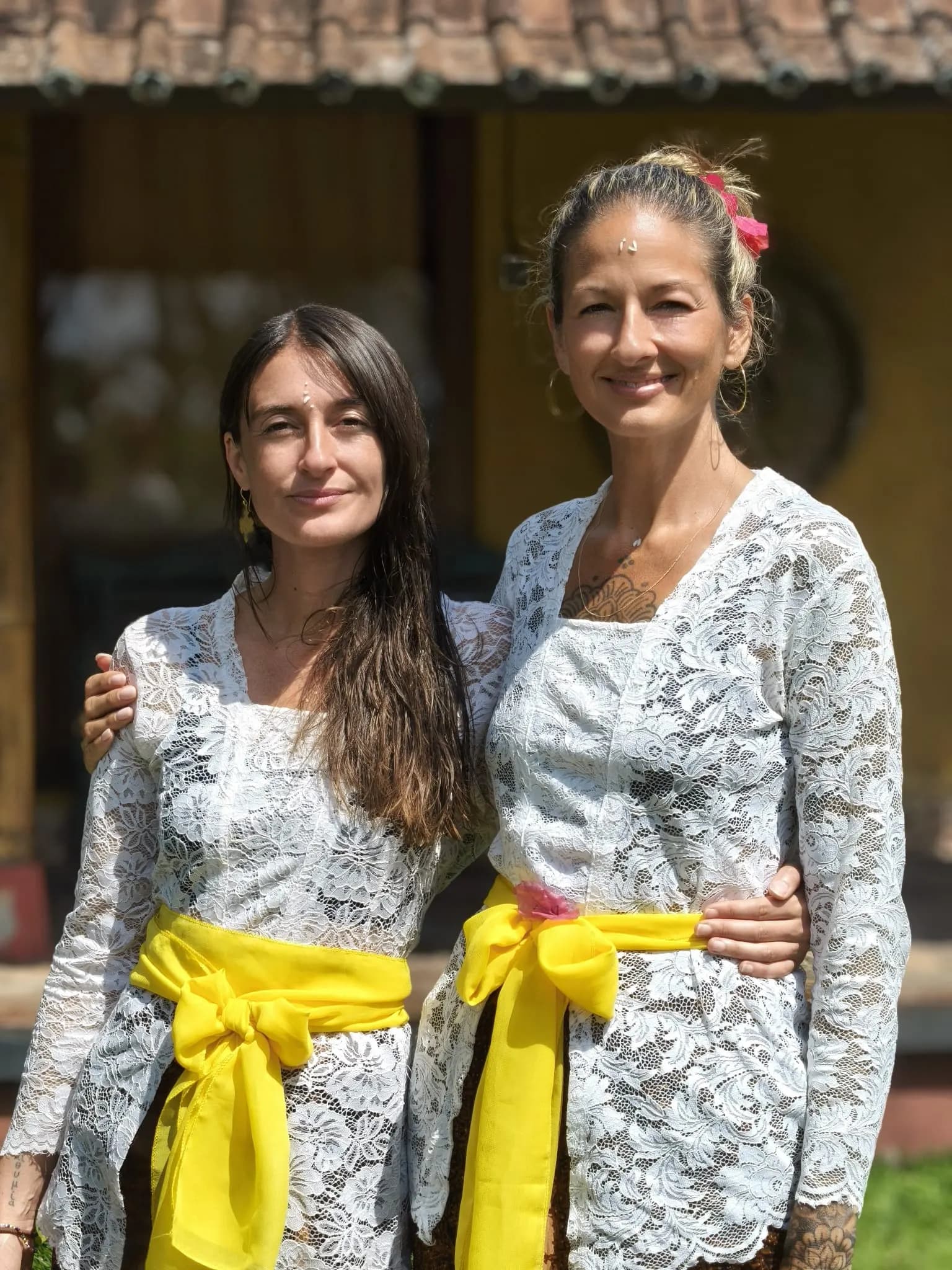 Two guests in lace kebaya and yellow sashes after a temple blessing