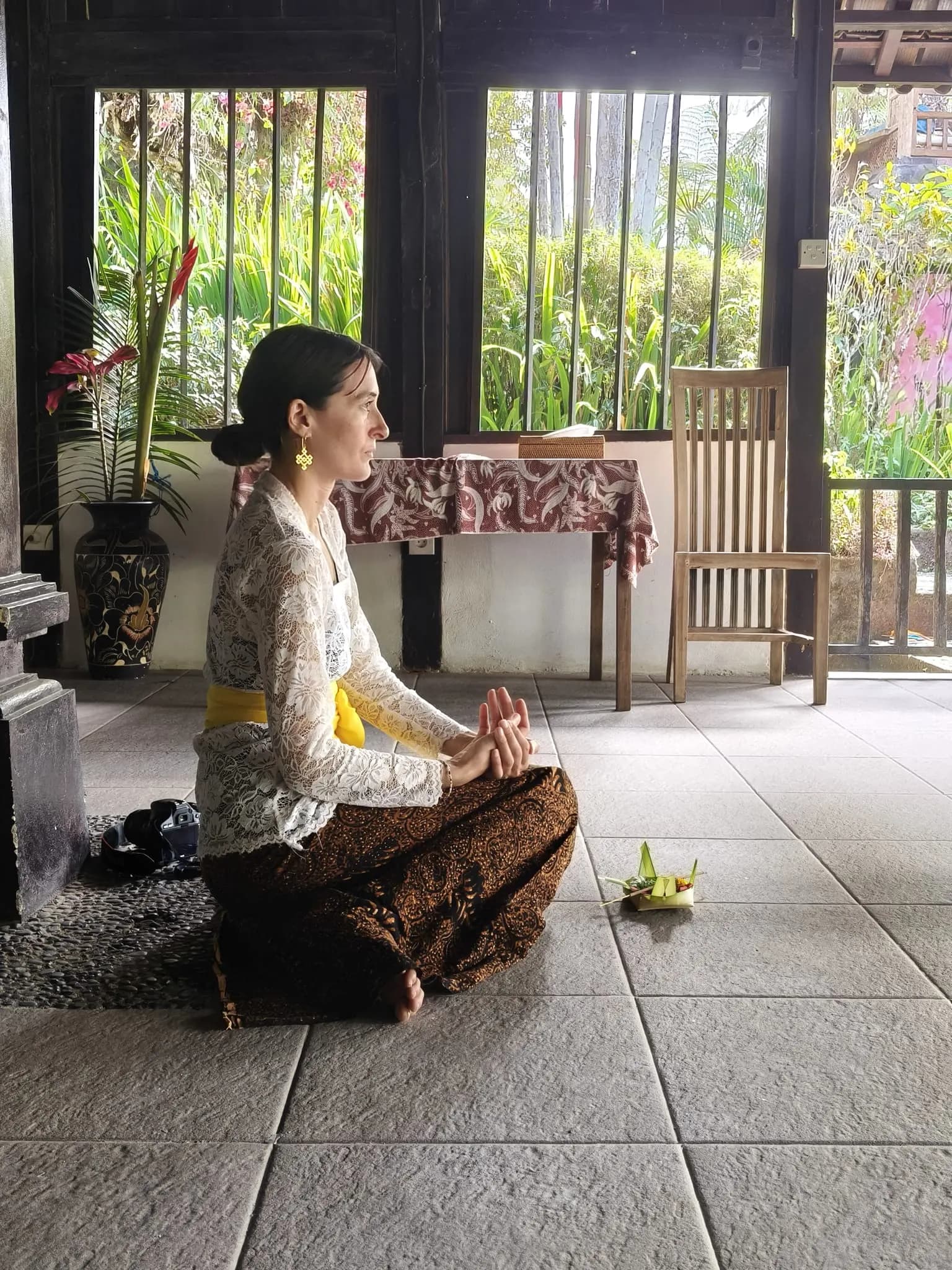 A guest in kebaya seated in prayer before a palm-leaf offering