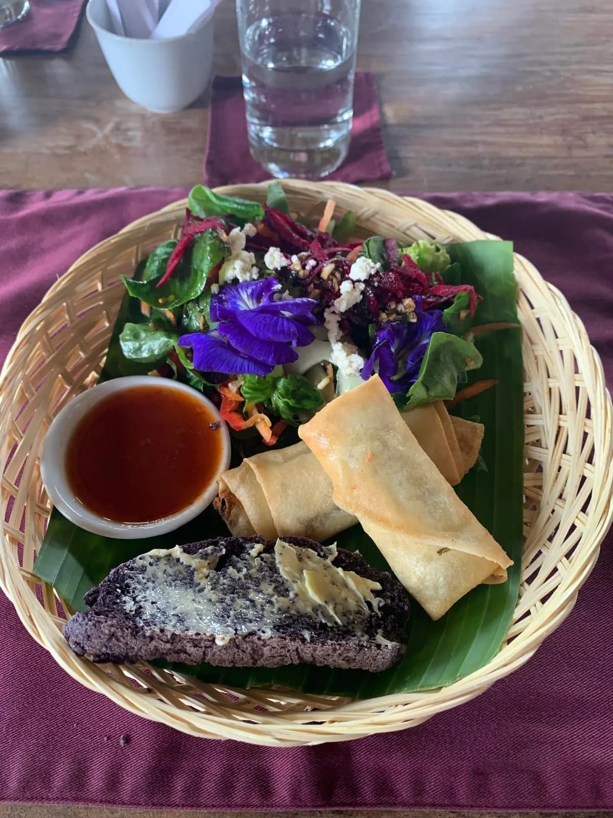 Garden salad with butterfly-pea flowers and crisp spring rolls in a rattan basket