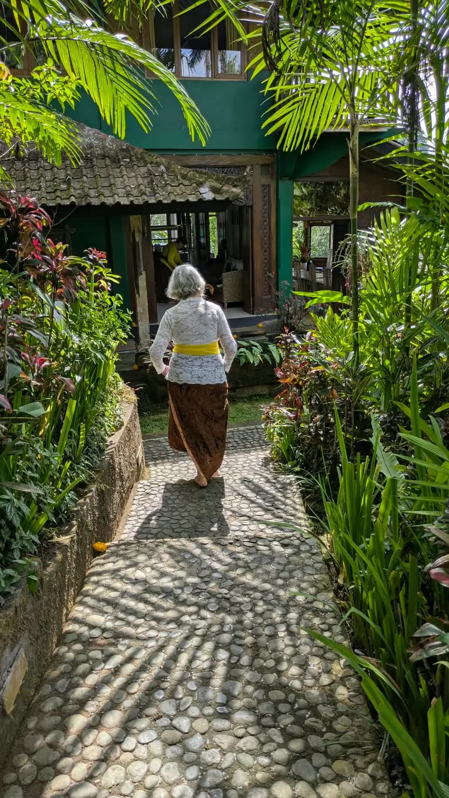 A sunlit river-stone path through the garden toward the restaurant