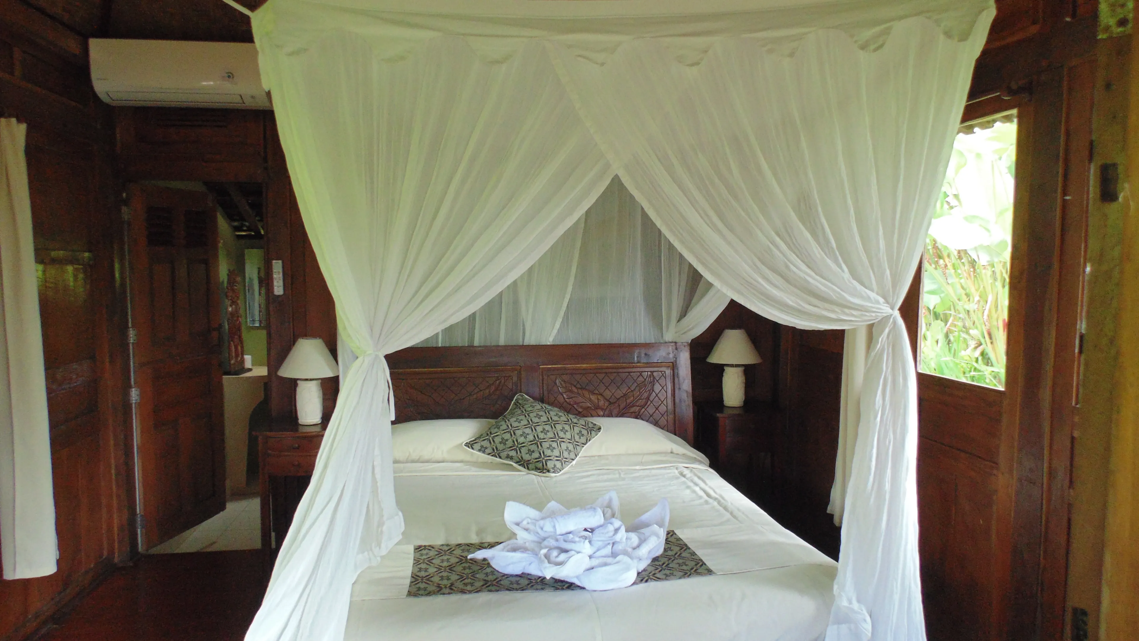 Netted bed with a carved teak headboard in the teak-panelled Gladak House
