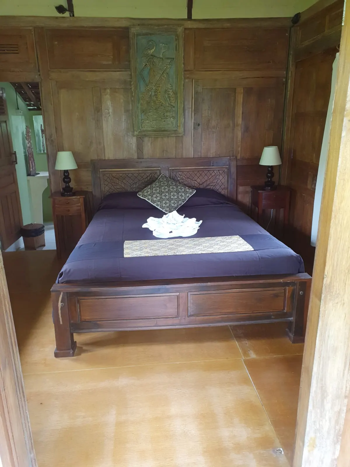 Teak-panelled Gladak House bedroom with a carved headboard and purple linen