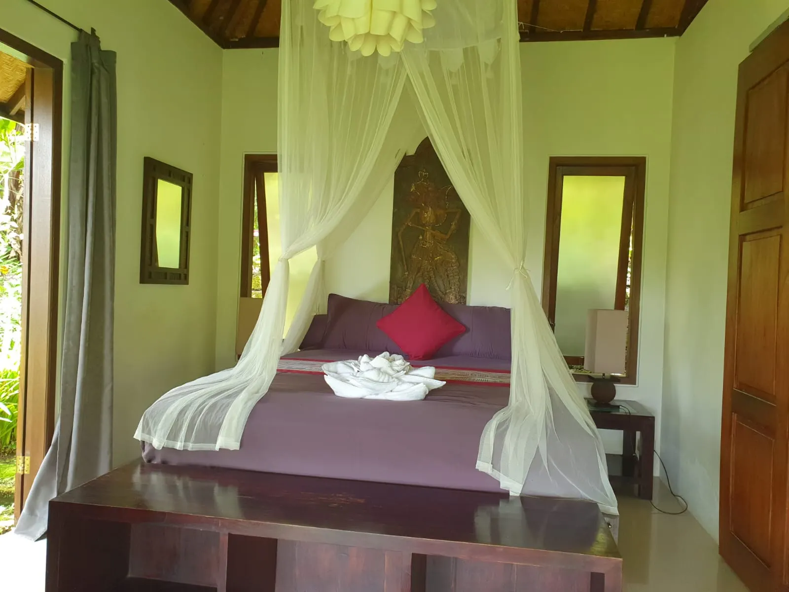 The Lotus House canopy bed with a red cushion beneath a carved wayang panel