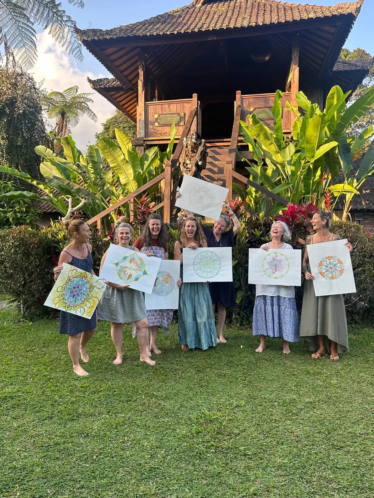 Retreat guests holding up their mandala paintings on the lawn before a raised timber house