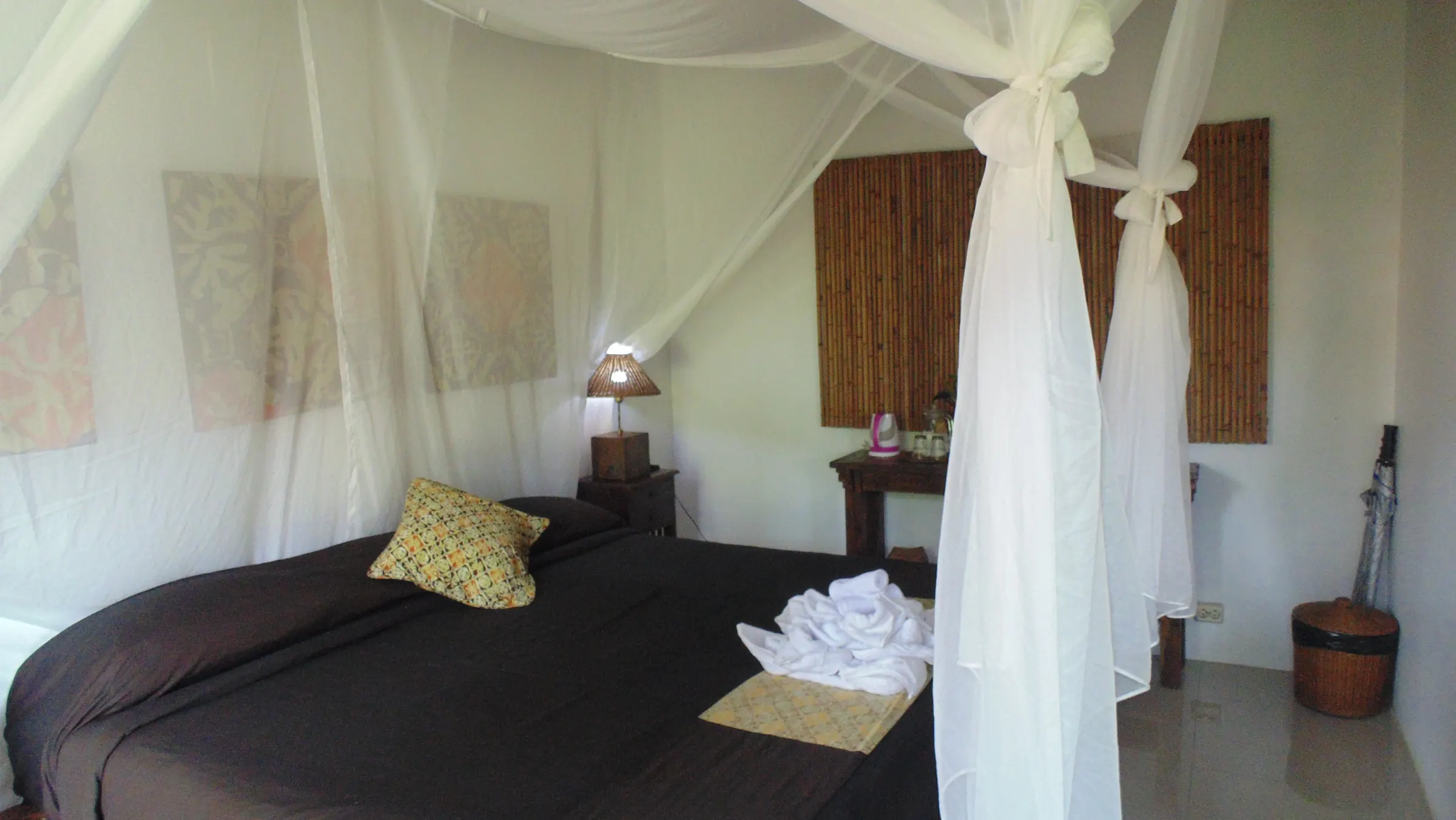 Canopy bed with a batik cushion and bamboo wall panel in the Superior Teak House