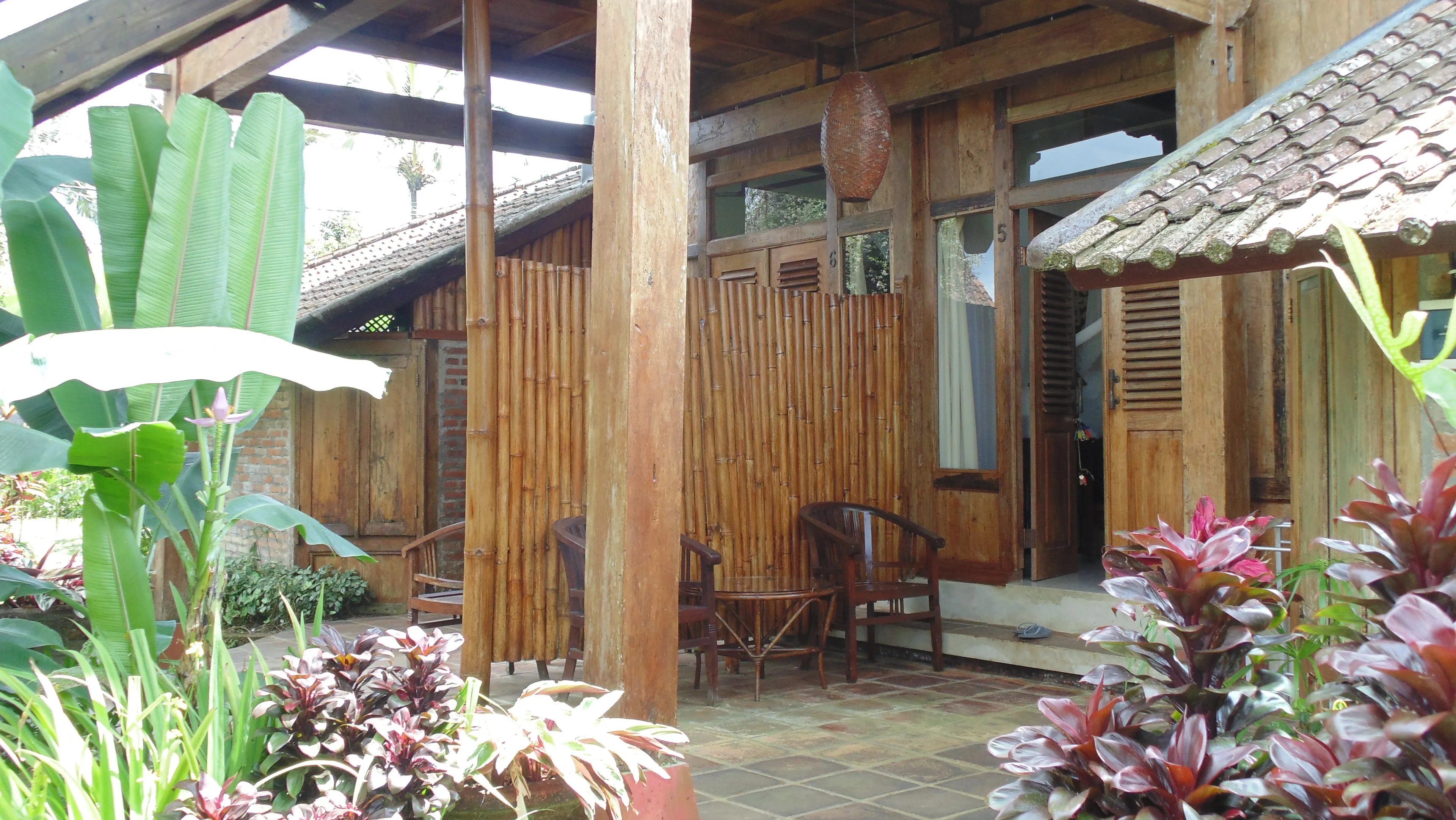 A bamboo-screened teak terrace framed by banana leaves and cordyline