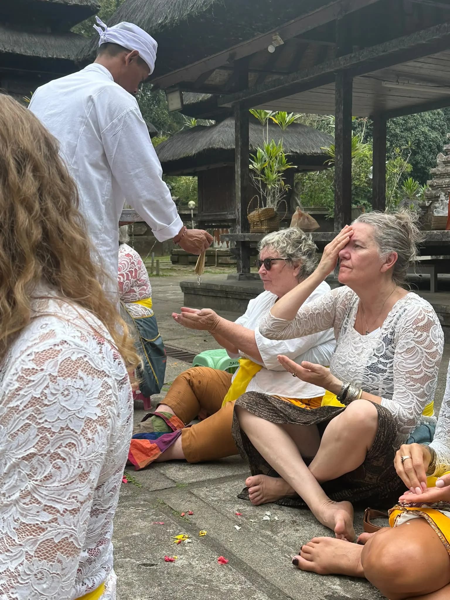 A temple priest pouring holy water into the cupped hands of guests in kebaya