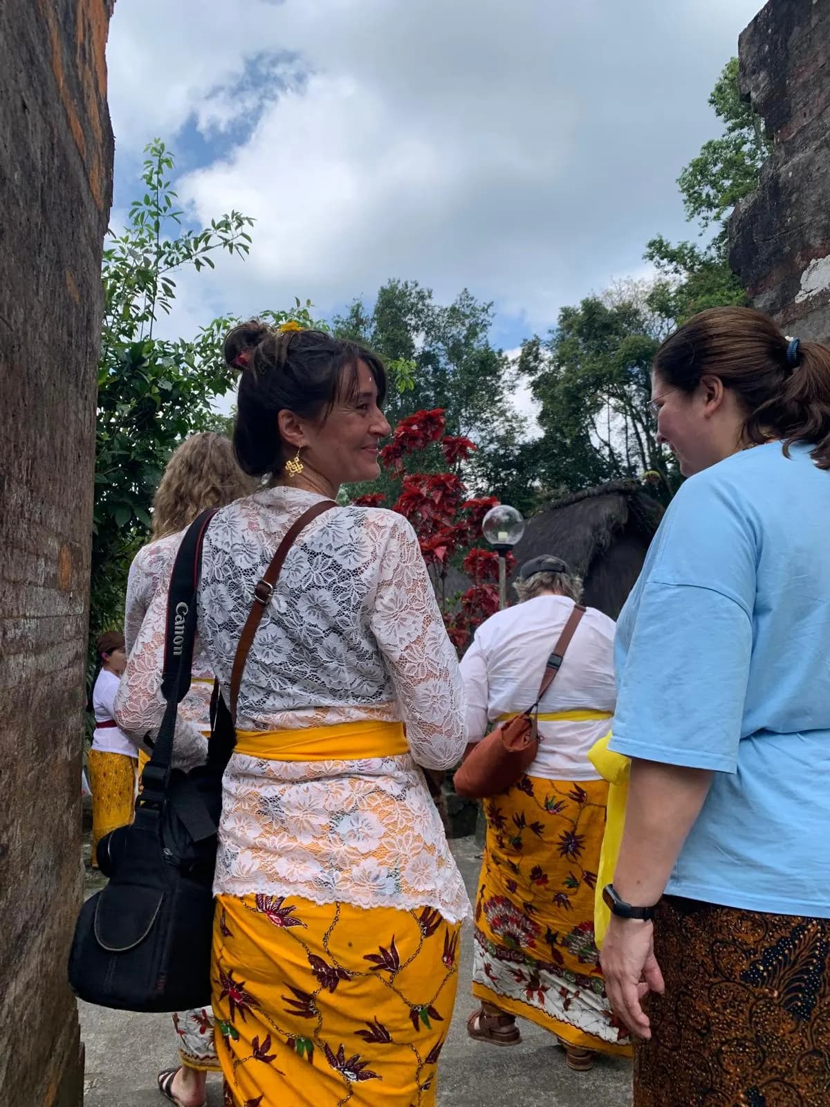 Walking through a stone temple gateway in lace kebaya and a yellow sarong