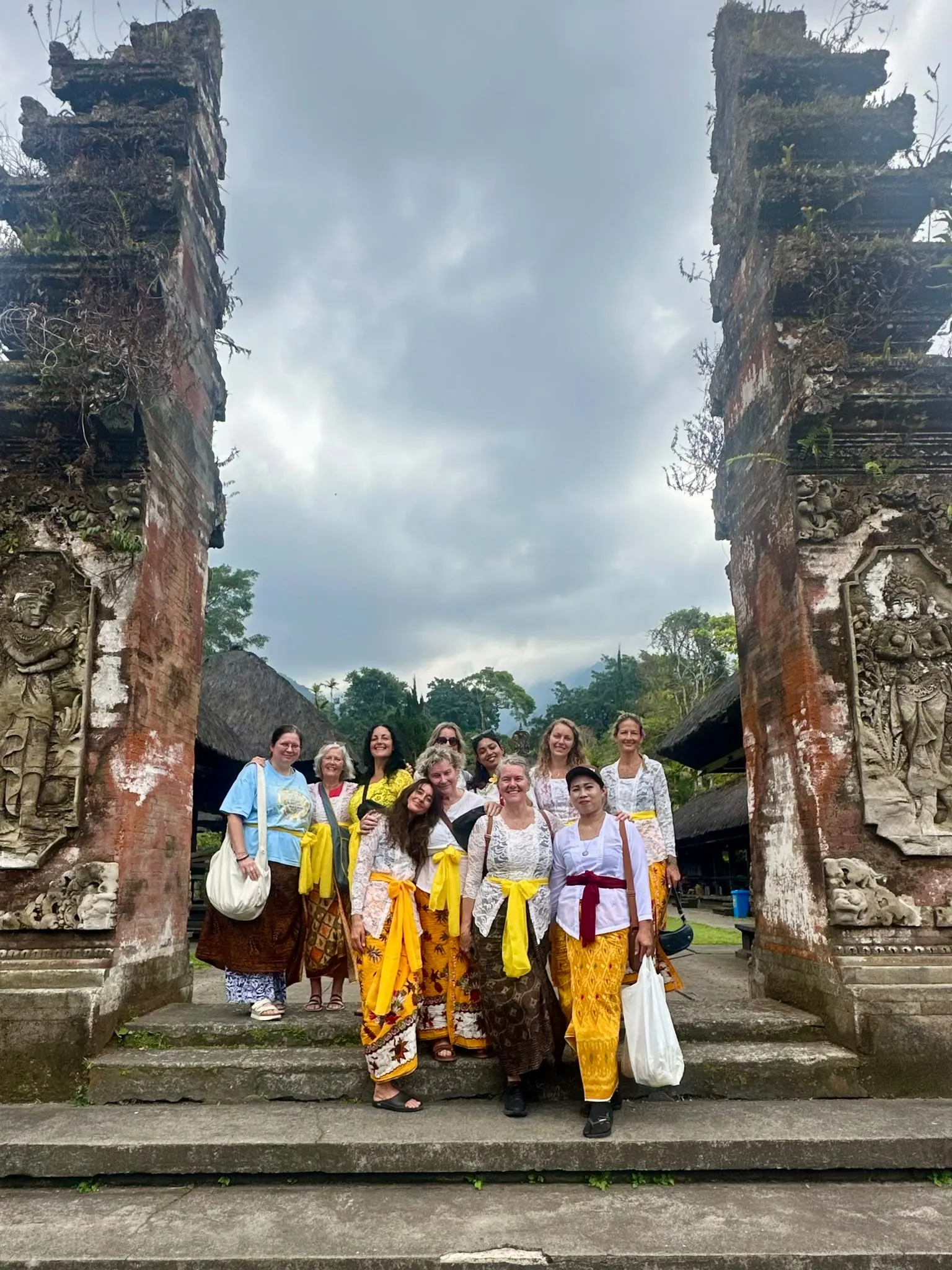 Guests in white lace kebaya on the steps of a mossy temple split gate