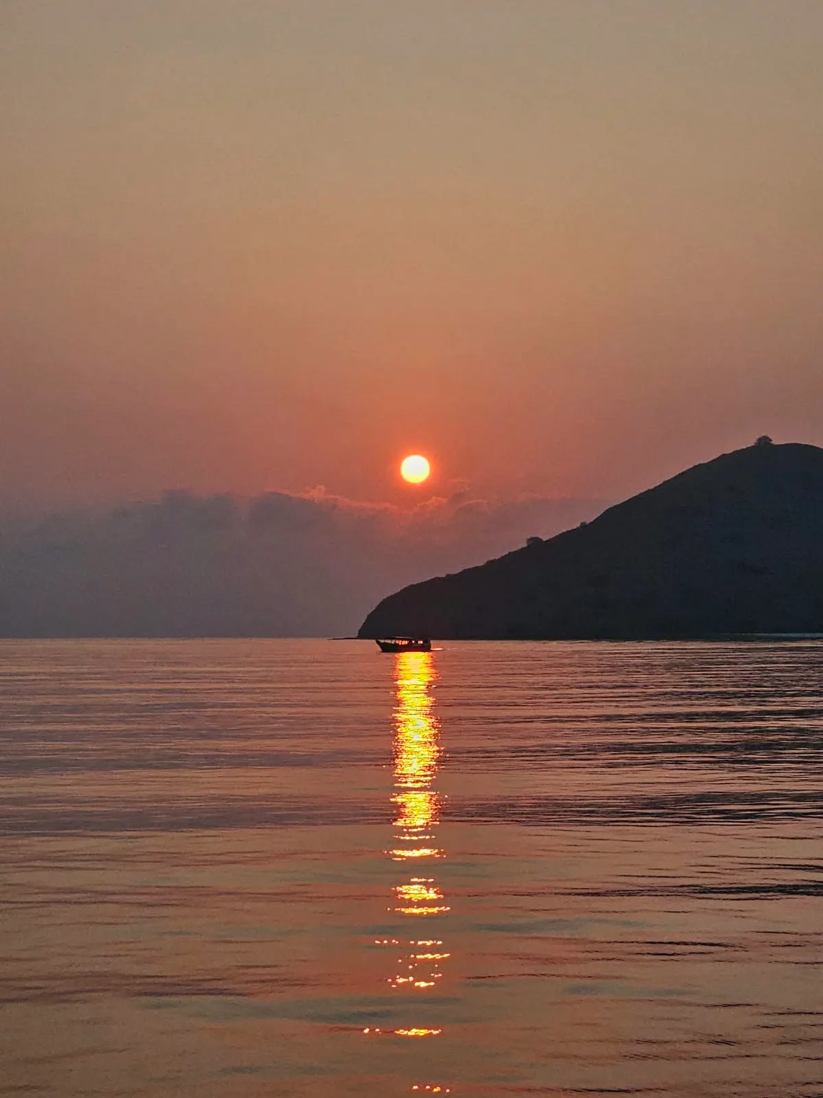 The sun setting over a calm sea beside a dark headland