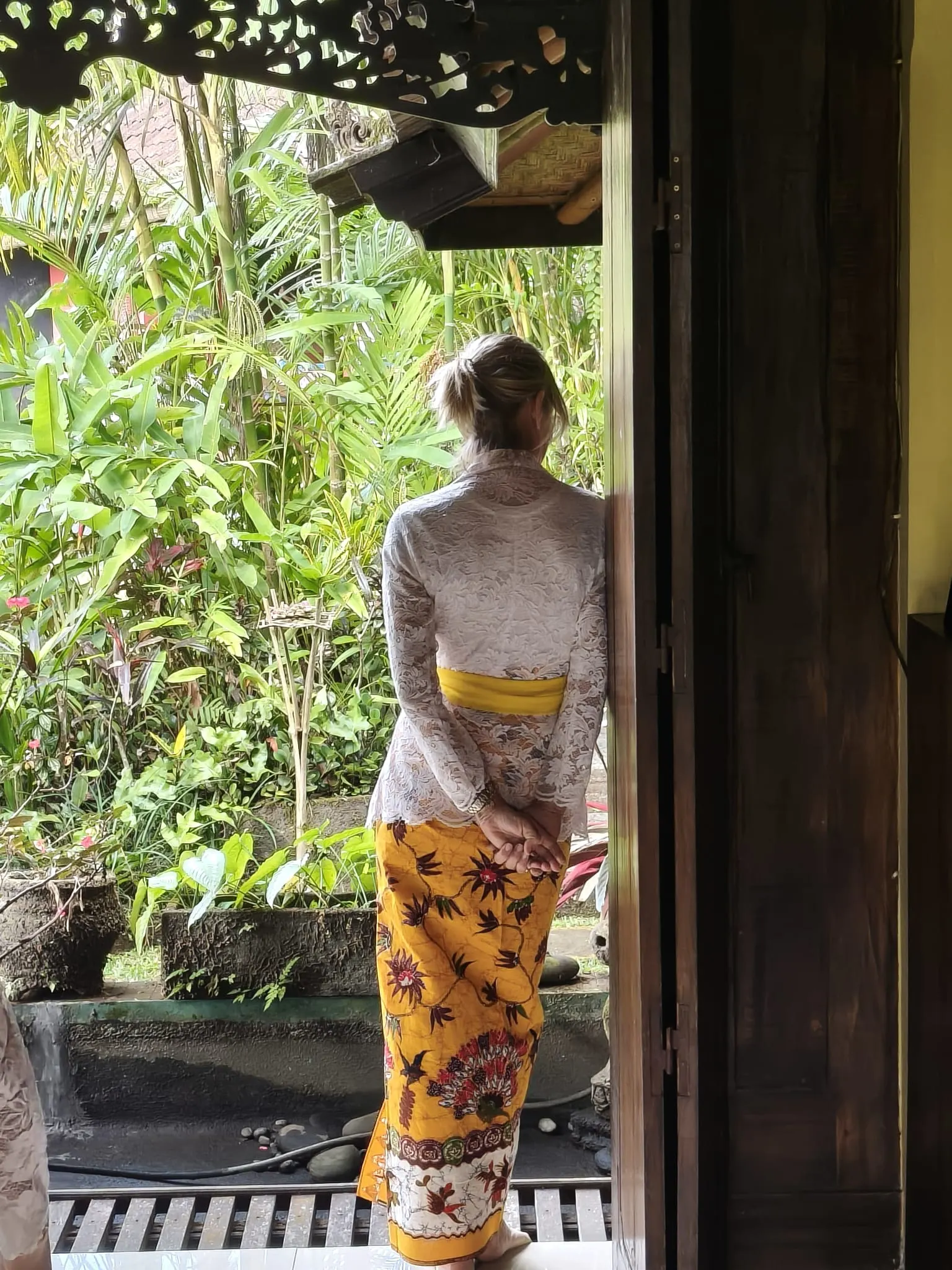 A guest in temple dress looking out from a carved timber doorway into the garden