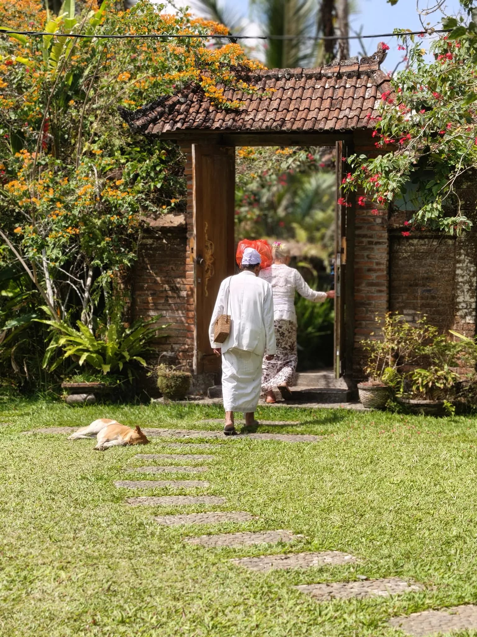 Carrying an offering through a carved garden gate in white temple dress