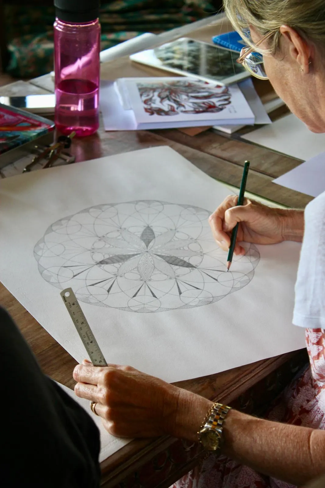 A hand drawing an intricate pencil mandala with a ruler